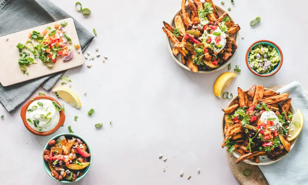 A table with bowls of healthy food, including sweet potato fries, guacamole, and fresh toppings, representing the discussion on Montmorillonite Clay in Dog Food Side Effects